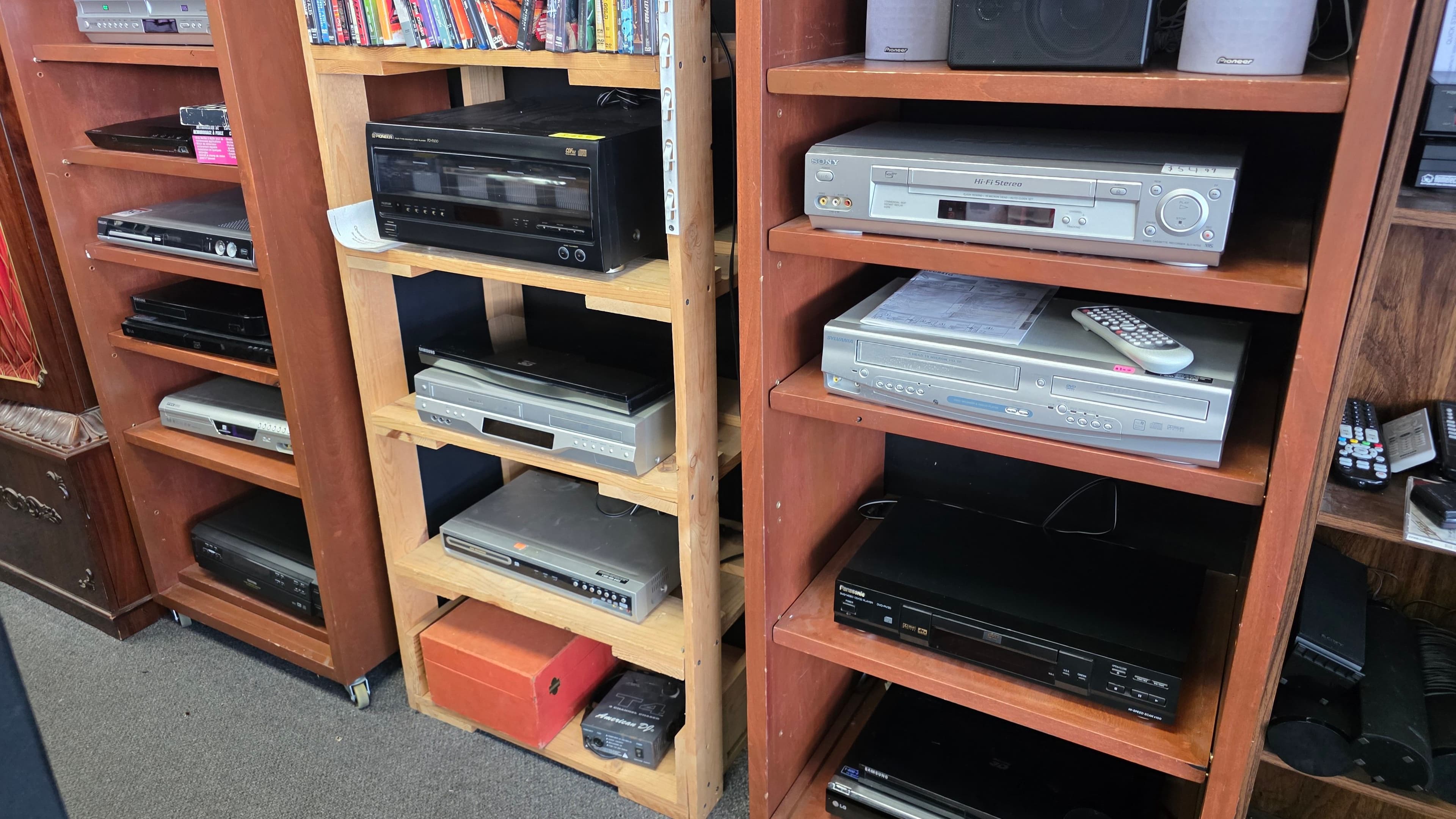 Wooden shelving racked with DVD players and VCRs, a Sony Hi-Fi VCR mid-shelf and Pioneer bookshelf speakers on top.