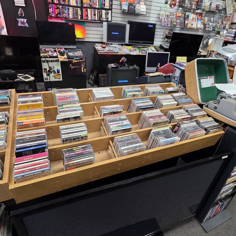 Rows of CD browser bins on a wood-topped counter, with CRT televisions and the VHS wall behind them.