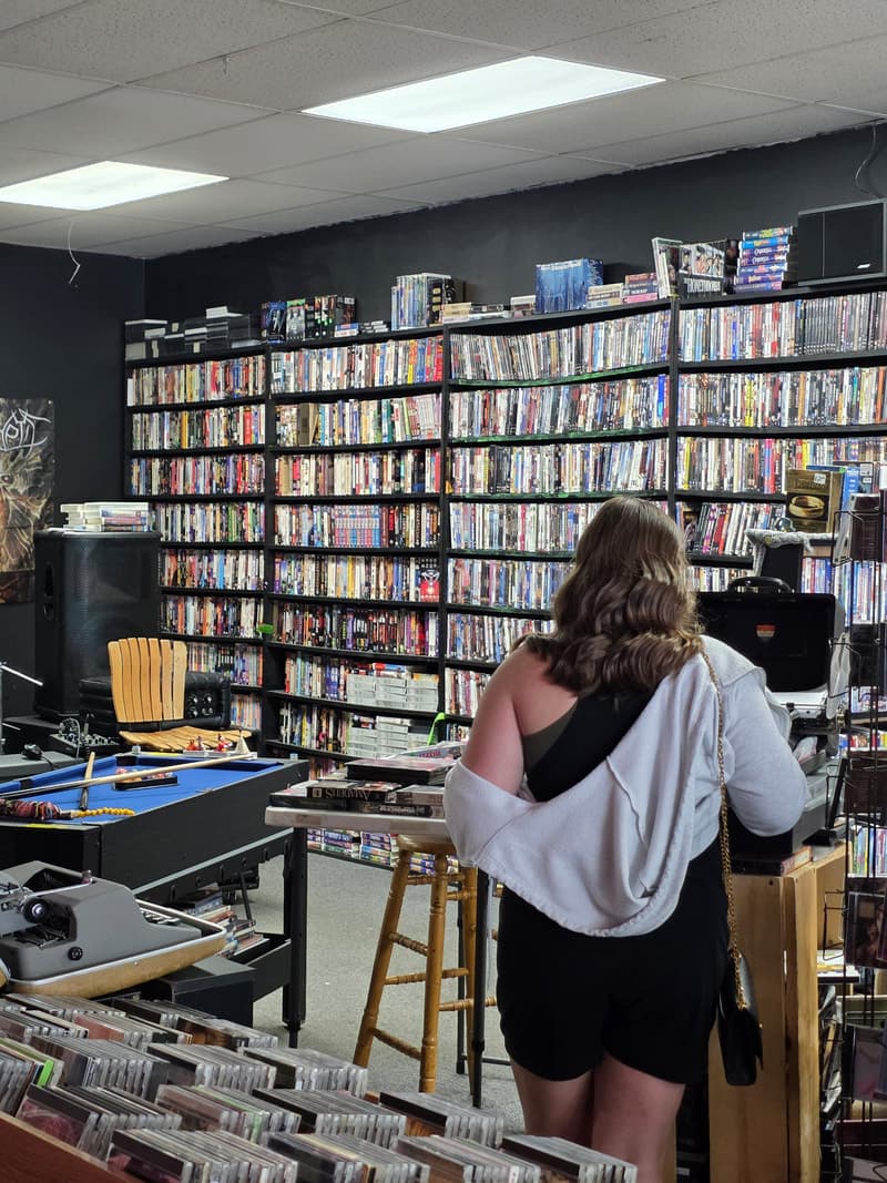 A customer at the counter in front of the full-height DVD wall, with a pool table and typewriter in the foreground.