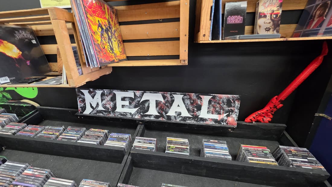 A hand-painted METAL sign above cassette bins, with vinyl crates and a red guitar below.