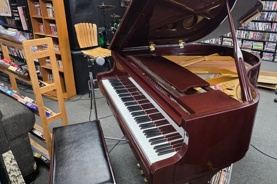 A mahogany baby grand piano with its lid open and a mic stand beside it, DVD shelving all around.