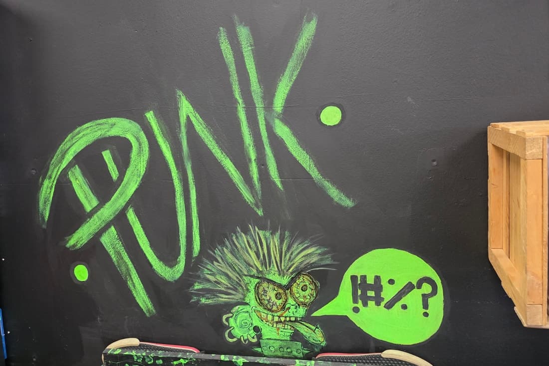 A green chalk PUNK mural with a spiky-haired cartoon character on the black wall above a skate deck.