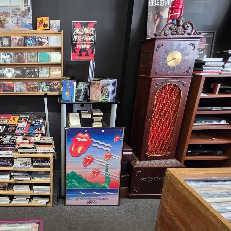 A Rolling Stones 1981 tour poster above cassette and 8-track bins, beside a grandfather clock.