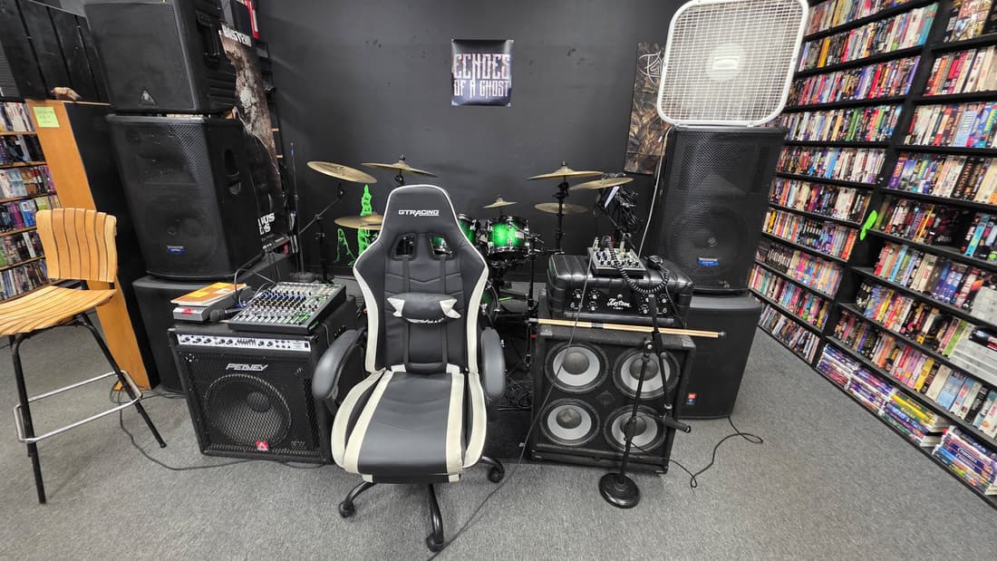 The stage corner between shows: drum kit, PA stacks and mixer against the black wall.