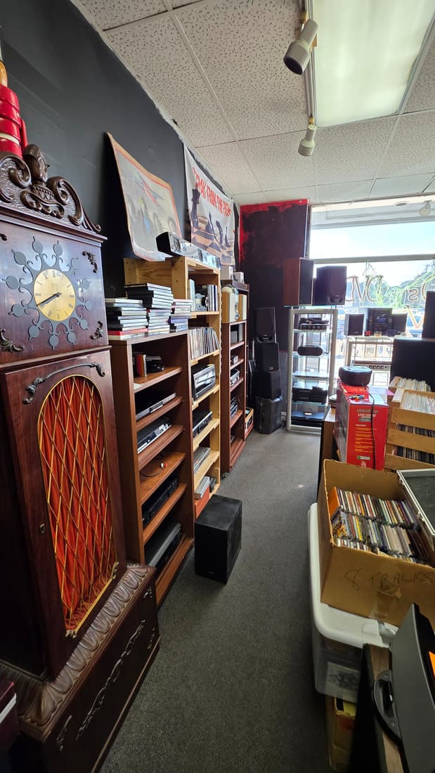 An aisle looking toward the front window past a grandfather clock, stereo components and a box of 8-tracks.