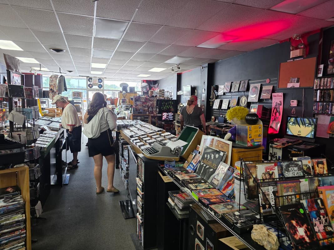 The shop floor mid-afternoon, customers browsing bins beneath a hand-lettered Media Cavern chalk sign.