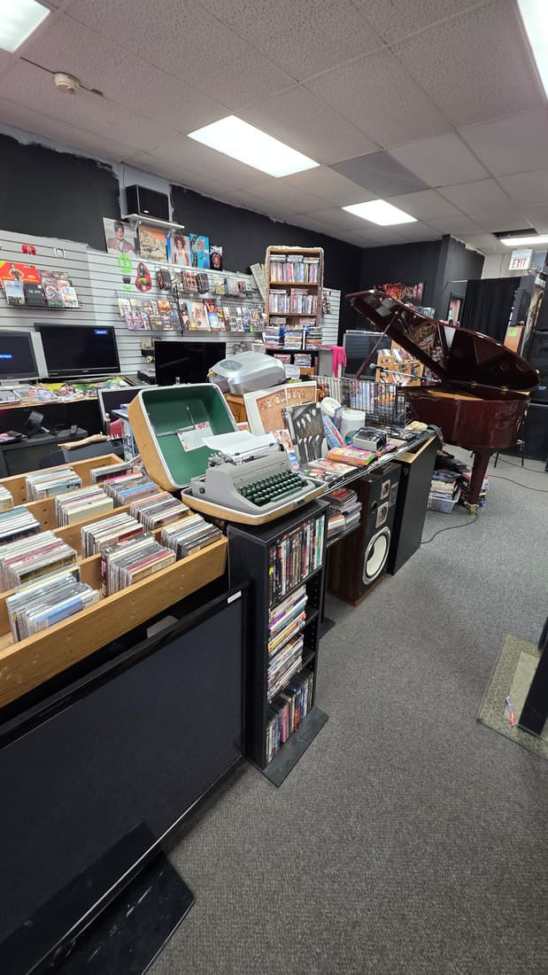 A tall view taking in the CD bins, a vintage typewriter, the grand piano and the slatwall in one frame.
