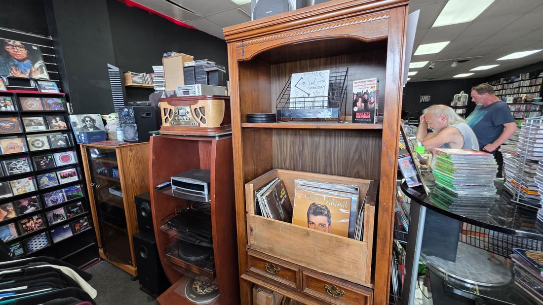 A vintage stereo console and turntable in a wooden hutch, components stacked beside it.